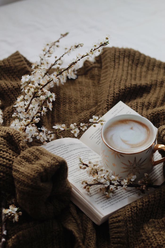 Warm coffee and an open book on a knitted sweater, adorned with delicate blossoms.